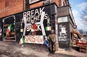 British Army black soldier standing in front of Republican mural of Margaret Thatcher and the hunger strikes in West Belfast during The Troubles, Northern Ireland Conflict. Belfast, 1982 PY1MDE