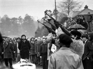 Three masked IRA men fire volleys of rifle shots over the coffin of hunger-striker Bobby Sands during a pause in the funeral procession en route to the Milltown cemetry, Belfast. Gerry Adams can be seen in background, wearing glasses and dufflecoat.
